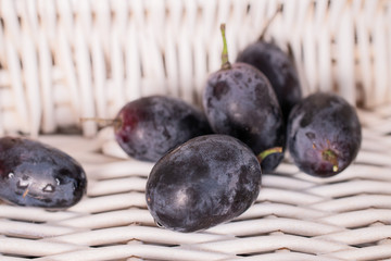 Group of six whole fresh black grape with braided rattan behind