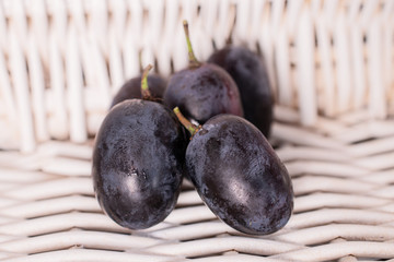 Group of five whole fresh black grape with braided rattan behind