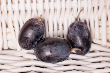 Group of three whole fresh black grape with braided rattan behind