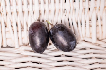 Group of two whole fresh black grape with braided rattan behind