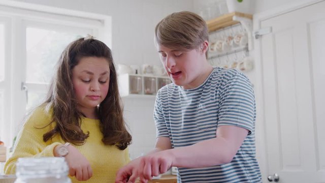 Young Downs Syndrome Couple Taking Homemade Cupcakes Out Of Baking Tray