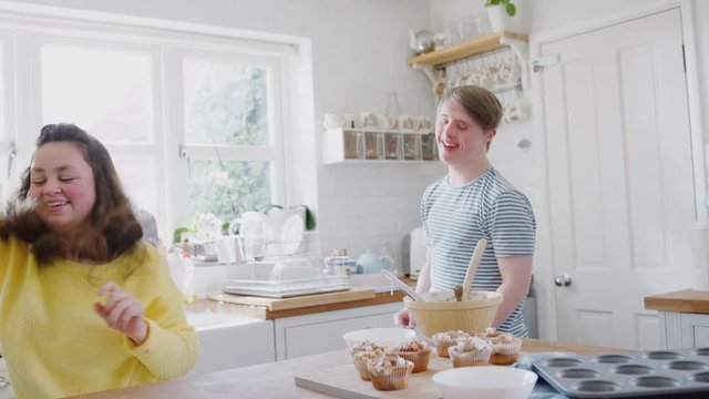 Young Downs Syndrome Couple Decorating Homemade Cupcakes And Dancing In Kitchen At Home