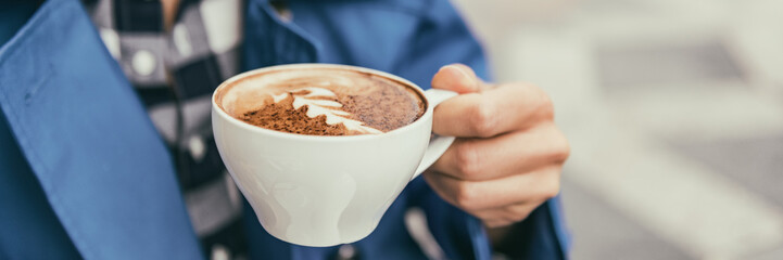 Coffee cup cappuccino woman drinking latte at outdoor cafe. Coffee shop city lifestyle banner panorama closeup of hand holding latte art cup.