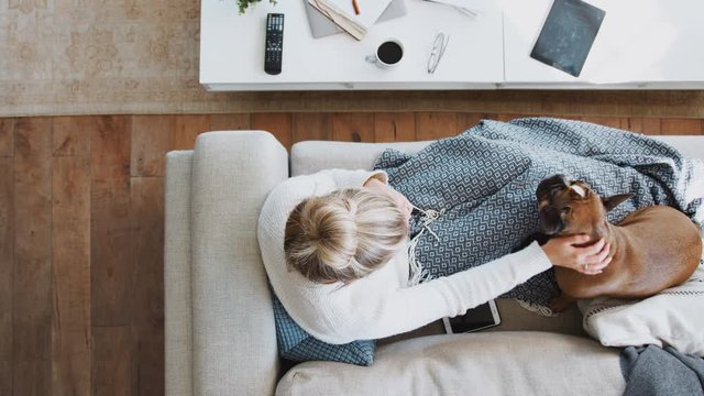 Overhead Shot Looking Down On Woman At Home Lying On Sofa Playing With Pet Dog