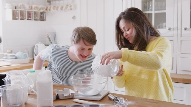 Young Downs Syndrome Couple Measuring Ingredients To Bake Cake In Kitchen At Home