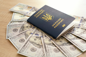 Obraz premium Ukrainian biometric passport and dollars on a wooden background. Money and documents for trip abroad. Documents for immigration.