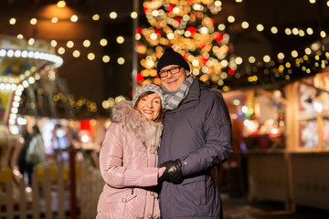 love, winter holidays and people concept - happy senior couple hugging at christmas market on town hall square in tallinn, estonia