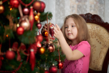 Fototapeta na wymiar A little girl wearing light pink dress decorating a Christmas tree.