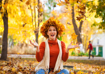 Young beautiful woman with a wreath of maple leaves posing in autumn park