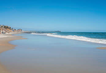 Wave crashes on sandy beach on a sunny, cloudless day