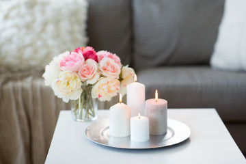 decoration, hygge and cosiness concept - candles burning on table and flowers at cozy home