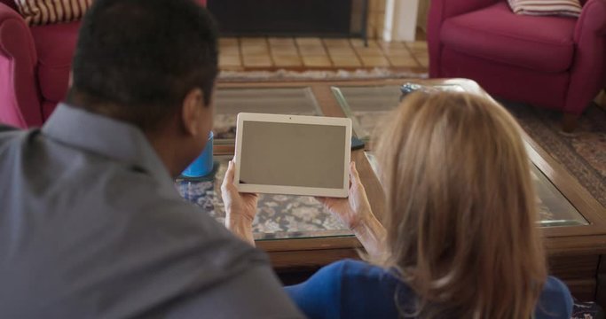 Over the shoulder shot of African American and Caucasian couple holding tablet computer with blank screen for compositing. Husband and wife looking at mobile device together. Slow motion 4k Handheld