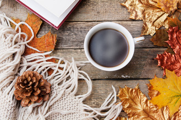 Autumn layout: hot coffee, book, golden autumn leaves, knitted sweater, plaid on a wooden table. Cozy autumn mood in October, November