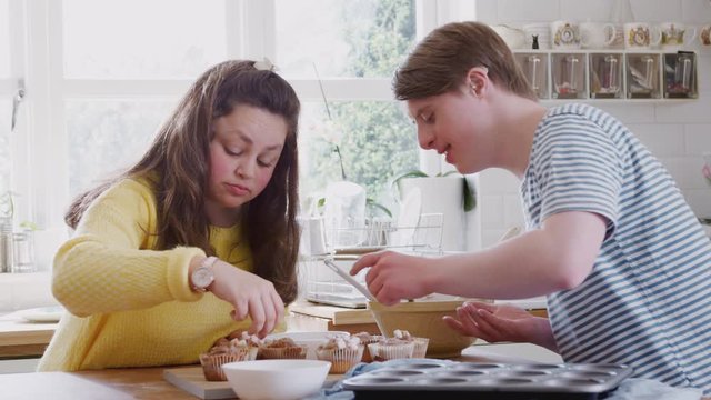 Young Downs Syndrome Couple Decorating Homemade Cupcakes With Marshmallows In Kitchen At Home