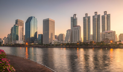 Skyscrapers and Lake with Wooden Walk Way in City Park. View of Benjakiti Park at Sunrise. Beautiful Morning Scene of Public Park in Bangkok, Thailand, Asia.