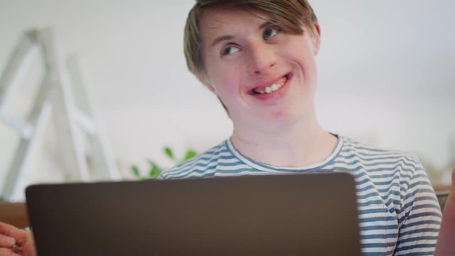 Young Downs Syndrome Man Sitting On Sofa Watching Laptop At Home And Dancing