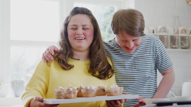 Portrait Of Downs Syndrome Couple Holding Homemade Cupcakes With Marshmallows In Kitchen At Home