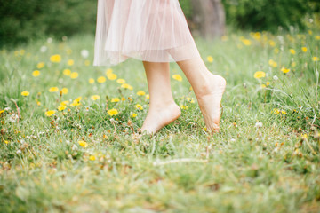 legs of young barefoot women wearing pink dress standing on one leg on green grass with yellow...