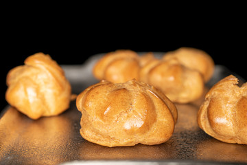 Lot of whole fresh baked golden profiterole on tray isolated on black glass