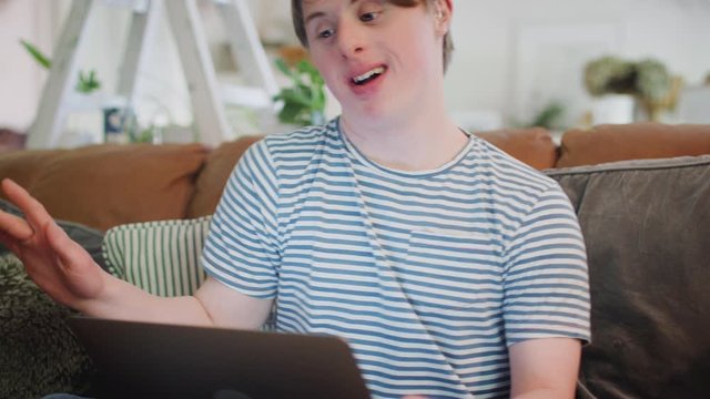 Young Downs Syndrome Man Sitting On Sofa Watching Laptop At Home And Dancing