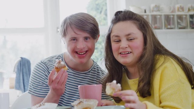 Portrait Of Young Downs Syndrome Couple Enjoying Tea And Cake In Kitchen At Home