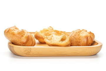 Group of three whole one half of baked golden profiterole on wooden square plate isolated on white background