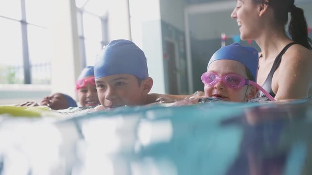Female Coach In Water With Children Gives Swimming Lesson In Indoor Pool
