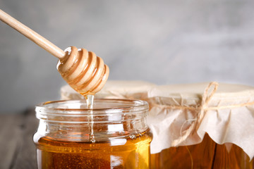 Pouring aromatic honey into jar, closeup. Honey in glass jars and honeycombs wax on wooden...