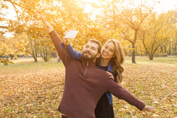Young couple using cellphone in autumn colored park.