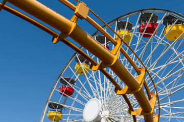 Colorful ferris wheel above a roller coaster track under a blue sky
