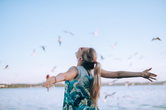 Girl stands on a background of the sky with seagulls spreading her arms