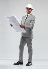 architecture, construction business and people concept - smiling indian male architect in helmet with blueprint over grey background