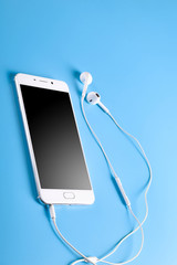  Mobile headphones and a mobile phone of white color on a blue background in light colors with a place for text.