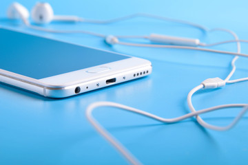  Mobile headphones and a mobile phone of white color on a blue background in light colors with a place for text.