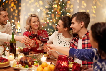 Fototapeta na wymiar holidays and celebration concept - happy friends having christmas dinner at home, drinking red wine and clinking glasses