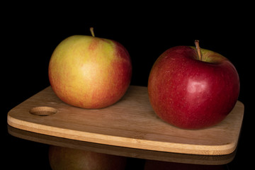 Group of two whole red apple jonagold on bamboo cutting board isolated on black glass