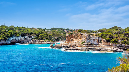 Fototapeta na wymiar Houses on cliffs around beautiful beach, Cala Llombards in Mallorca, turquoise water and blue sky, Balearic Island, Spain