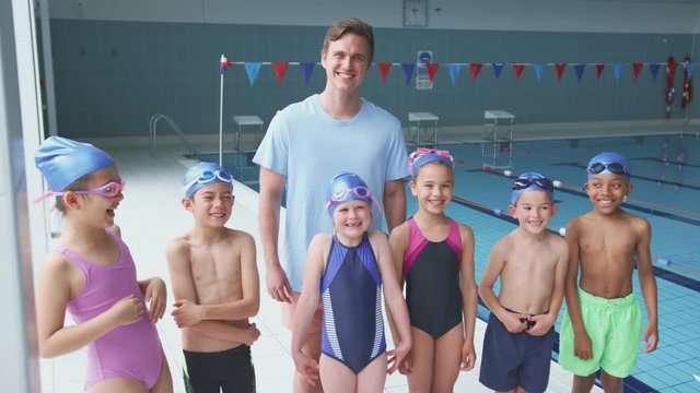 Portrait Of Children Standing By Edge Of Swimming Pool With Male Coach For Lesson