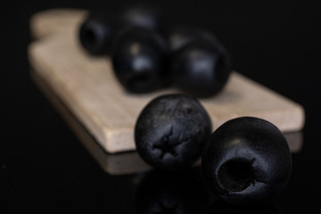 Group of seven whole tasty black olive on wooden board isolated on black glass