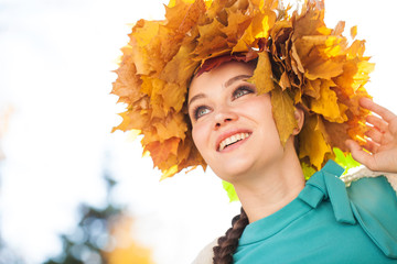 Young beautiful woman with a wreath of maple leaves posing in autumn park