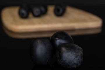 Group of eight whole tasty black olive on bamboo cutting board isolated on black glass