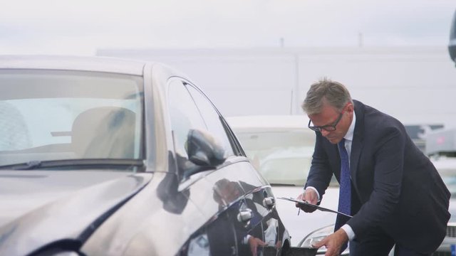 Insurance Loss Adjuster With Clipboard Inspecting Damage To Car From Motor Accident