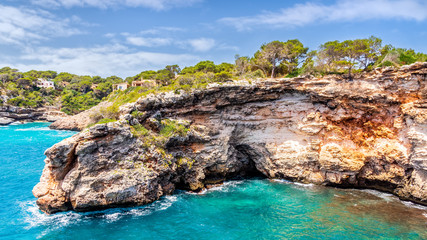 Fototapeta na wymiar Houses on cliffs around beautiful beach, Cala Llombards in Mallorca, turquoise water and blue sky, Balearic Island, Spain