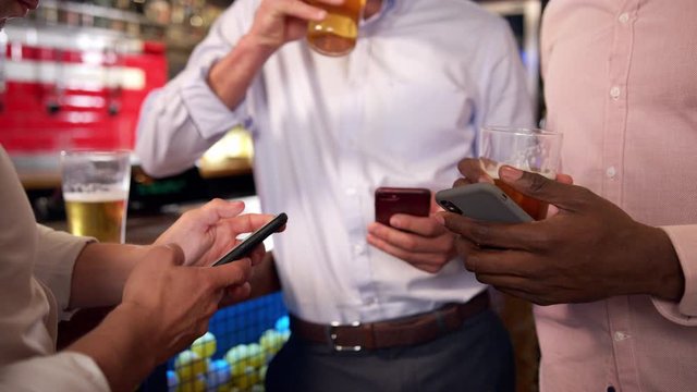 Group Of Businessmen All Checking Mobile Phones Whilst Meeting For Drink In Bar