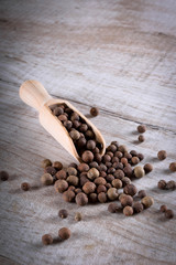 Pepper peas in a wooden spoon on a wooden background. Spices are scattered on the table