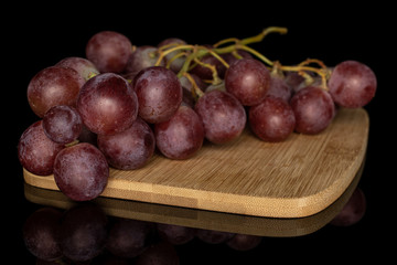 Lot of whole fresh purple grape rose on bamboo cutting board isolated on black glass
