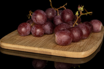 Lot of whole fresh purple grape rose cluster on bamboo cutting board isolated on black glass