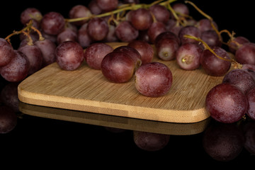 Lot of whole fresh purple grape rose on bamboo cutting board isolated on black glass