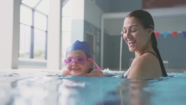 Female Swimming Coach Giving Girl Holding Float Lesson In Pool