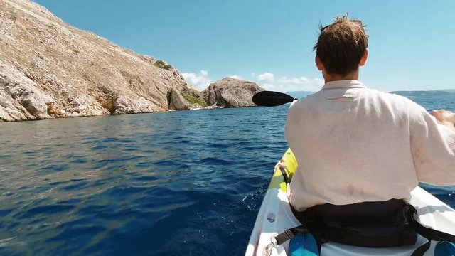 Young man paddling with a canoe next to sea cliffs at island coast of krk croatia beautiful water and sun